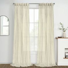 a living room with white curtains and a mirror on the wall next to a fireplace