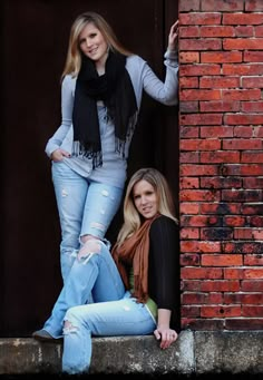 two beautiful young women standing next to each other in front of a red brick wall