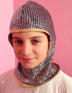 a young boy wearing a helmet and scarf on top of his head in front of a pink wall