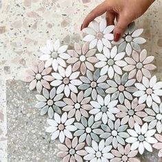 two hands are holding some white and pink paper flowers on the floor, while another hand is pointing at it