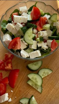 a glass bowl filled with cucumbers, tomatoes and feta cheese on top of a wooden table