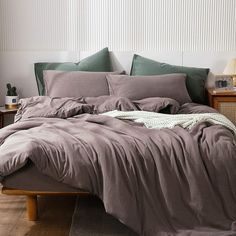 an unmade bed with purple sheets and pillows