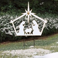 a metal nativity scene in the grass with snow on the ground and bushes behind it