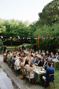 a large group of people sitting at tables in the middle of a yard eating food