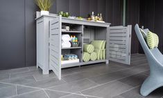 a grey cabinet with towels and soaps on it next to a chair in a room