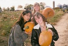 three girls holding pumpkins in their hands and posing for the camera on a farm path