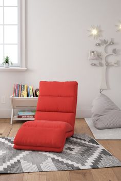 a red recliner chair sitting on top of a rug next to a book shelf