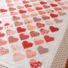 a quilted table topper with hearts on it, sitting on a wooden floor