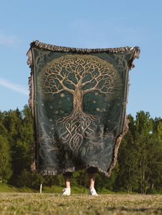 a person holding up a blanket with a tree on it in the middle of a field