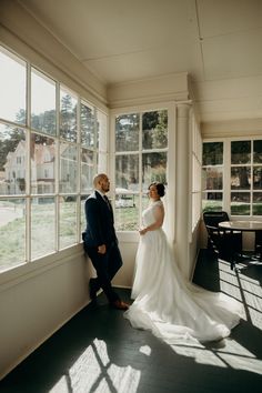 a bride and groom standing in front of a large window looking out at the yard