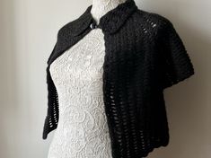 a white mannequin wearing a black crochet cardigan on top of a dress