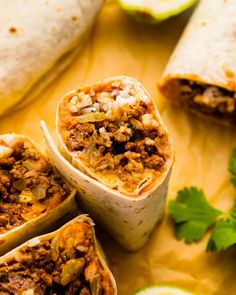 three burritos cut in half on a cutting board with cilantro and lime