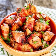 bacon wrapped chicken is served in a bowl with a fork and garnished with parsley