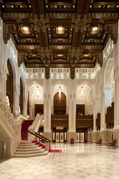 an ornately decorated lobby with stairs and chandeliers on the ceiling is lit by recessed lights