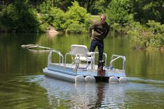 a man standing on top of a small boat in the middle of water with trees behind him