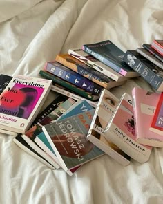 a pile of books sitting on top of a white bed next to eachother