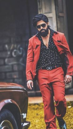 a man in red pants and a black shirt is standing next to an old car