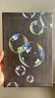 a person holding up a painting with soap bubbles on the bottom and black back ground