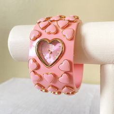 a pink watch with hearts on it sitting on top of a white rail next to a wall