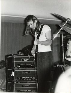 black and white photograph of a man playing guitar on stage with other instruments in the background