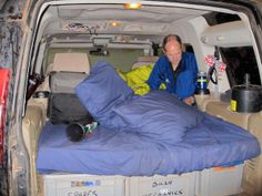 a man sitting in the back of a van with his bed pulled up to it