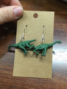 a pair of green dinosaur earrings sitting on top of a wooden table