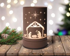 a lit candle with a nativity scene on it next to a pine branch and christmas lights