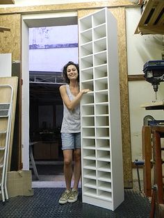 a woman standing next to a book shelf in a room with unfinished walls and flooring