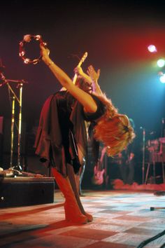 a woman is performing on stage with her hands in the air