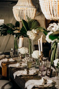 the table is set with white flowers and greenery in vases, candles and plates