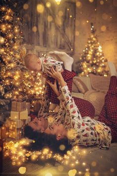 a woman laying on the floor with a baby in her lap next to a christmas tree