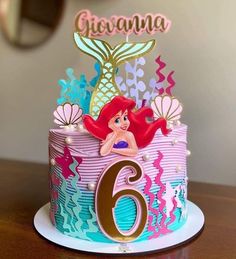 a birthday cake with the number six on it and ariel the mermaid topper in gold