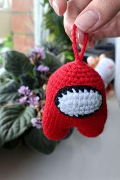 a hand holding a crocheted red object with white and black eyeballs on it