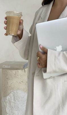 a woman is holding a cup of coffee and looking at her macbook air pro