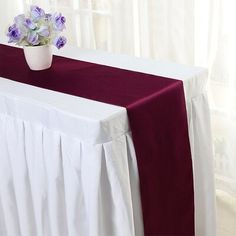 a red and white table cloth with purple flowers in a vase on the top of it