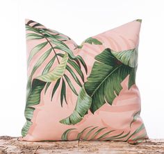 a pink pillow with palm leaves on it sitting on a piece of drifty wood