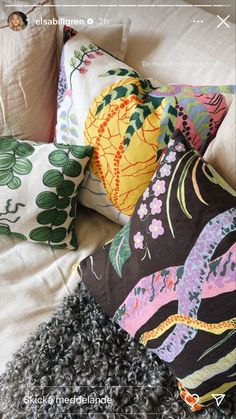 pillows and blankets are arranged on a bed with floral designs in black, pink, green, yellow and white