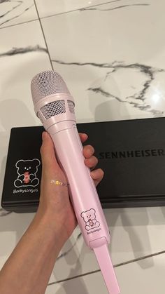 a person holding a pink microphone in front of a black box on a marble surface