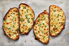 four pieces of bread with cheese and green onions on it sitting on a baking sheet