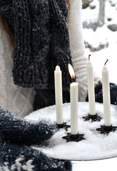 a woman holding a cake with candles on it in front of snow covered rocks and trees