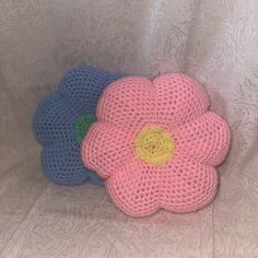 two crocheted flower pillows sitting on top of a white cloth covered bed sheet