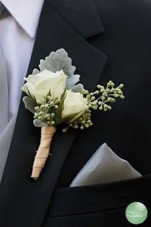 a boutonniere with white flowers and greenery attached to the lapel