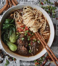 a bowl filled with noodles, meat and veggies on top of a newspaper