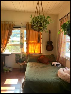 a bedroom with a bed, guitar and plants hanging from the ceiling in front of a window