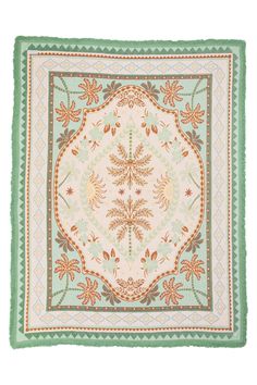 a green and white square rug with an ornate design on the center, surrounded by leaves