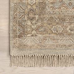 an area rug with fringes on top of a wooden floor next to a plant