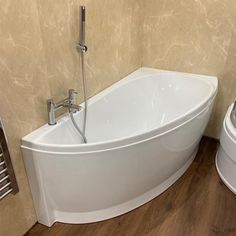 a white bath tub sitting next to a toilet on top of a hard wood floor