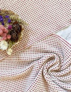 a basket with flowers on top of a white cloth covered in crocheted material