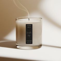 a white candle with a black label on it sitting in front of a light background