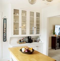 a bowl of fruit sitting on top of a wooden counter next to a white cabinet